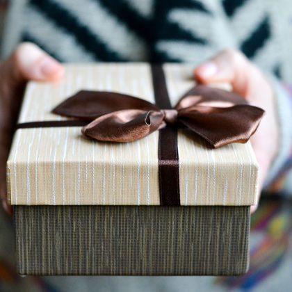 Gift box with brown ribbon held in hands